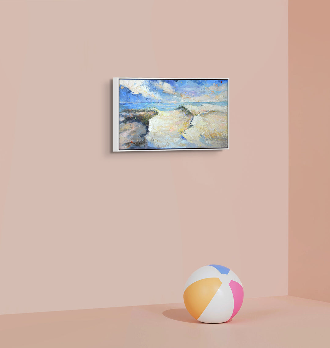 Framed coastal landscape painting of a beach and ocean on a wall.